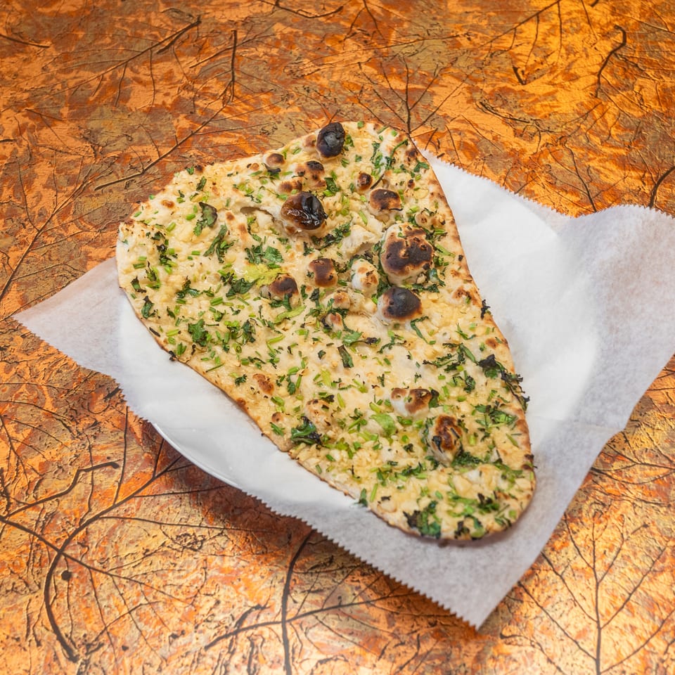 Grilled flatbread topped with herbs, melted cheese, and olives on parchment paper over a rustic wooden table.