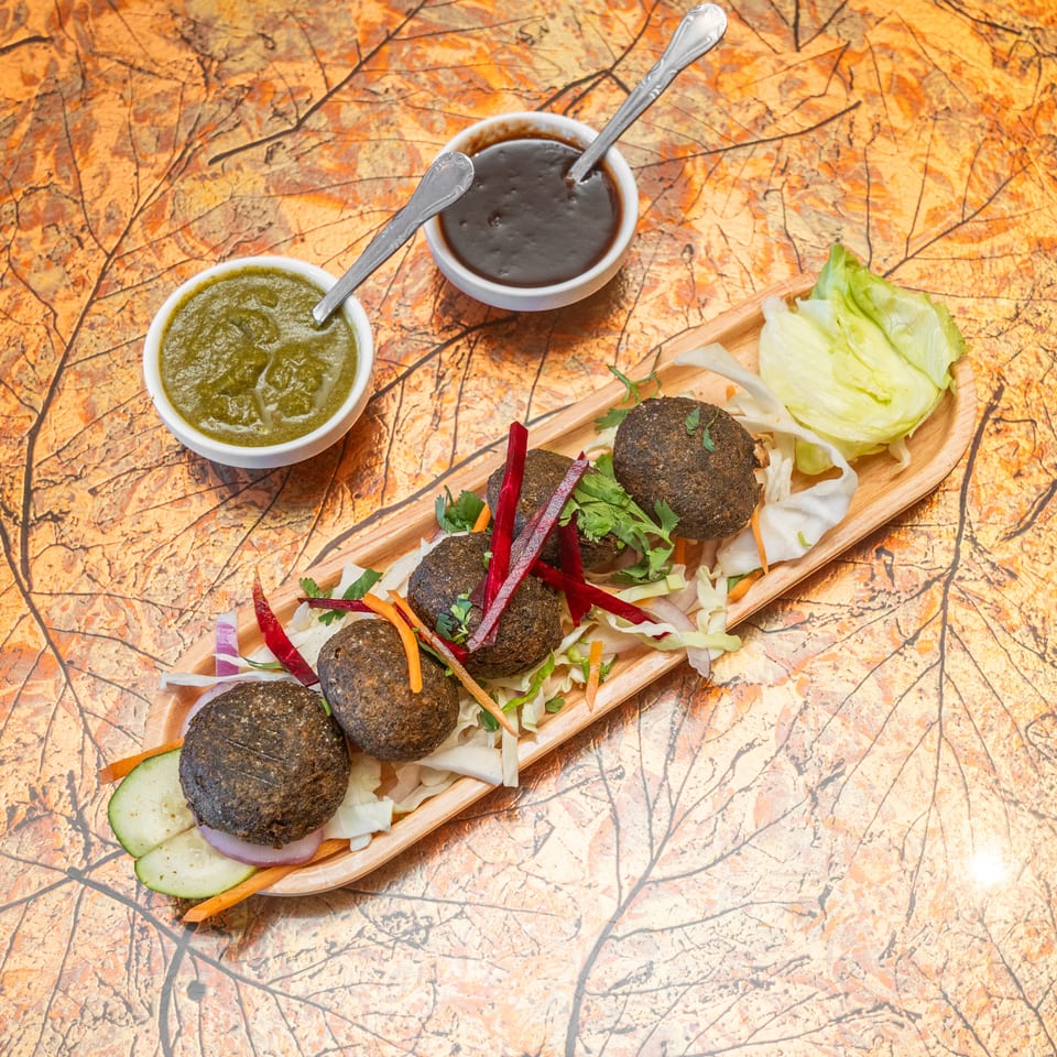 Falafel balls arranged with shredded salad, lettuce, herbs, and vegetables beside bowls of green and dark dipping sauces.