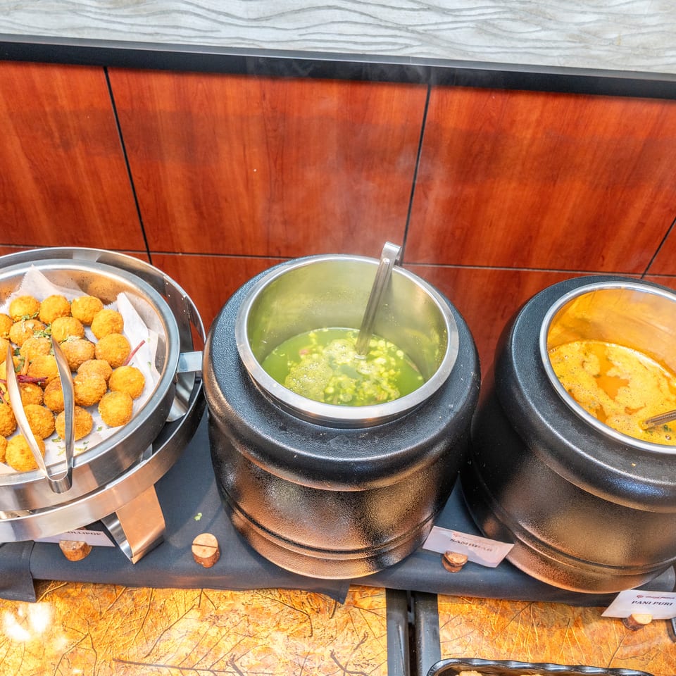 Buffet display with crispy fried bites, green chutney, and orange curry in serving dishes.