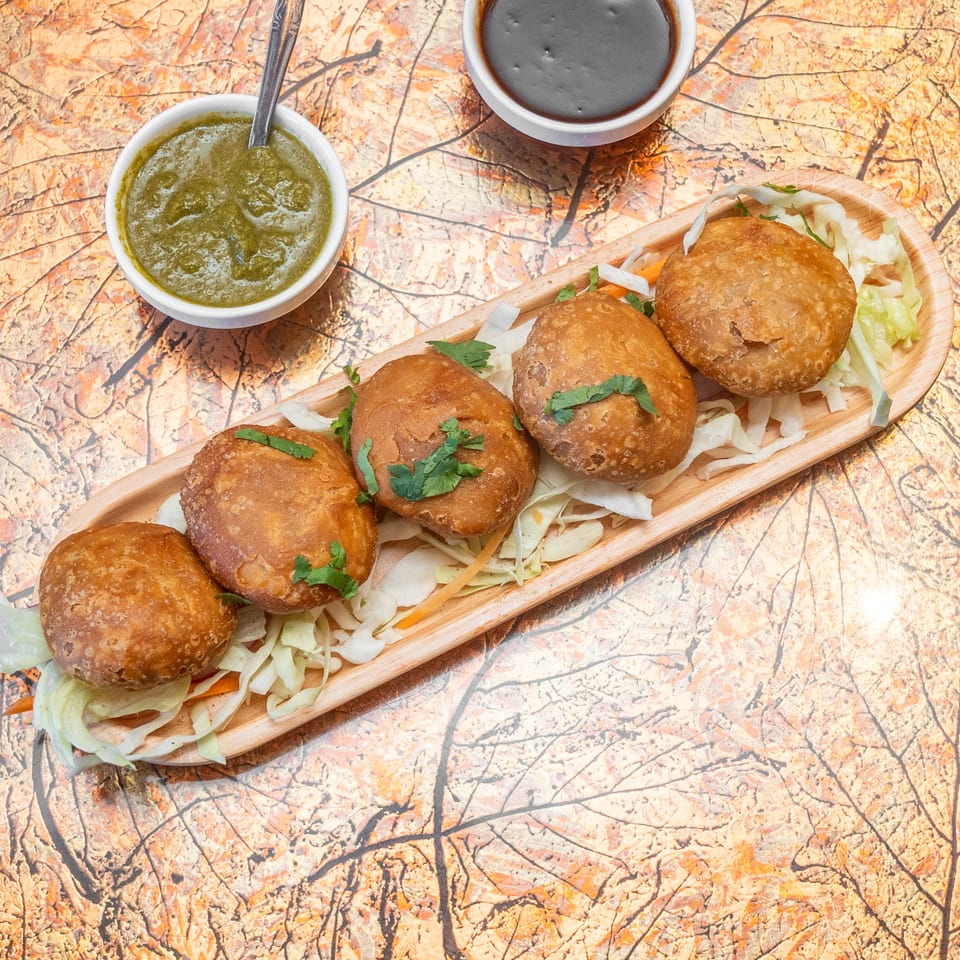 Crispy golden stuffed pastries served on shredded cabbage with cilantro, green chutney, and dark dipping sauce.