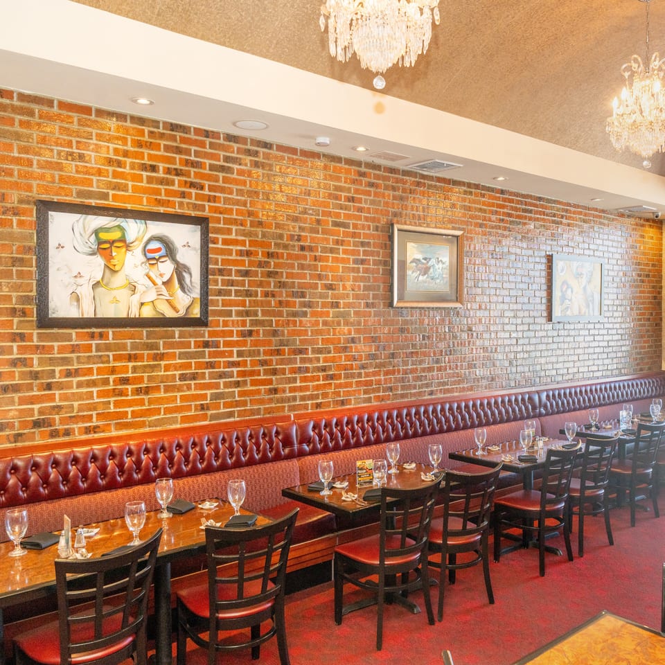 Elegant restaurant dining room with brick walls, framed artwork, crystal chandeliers, leather banquettes, and neatly set tables.
