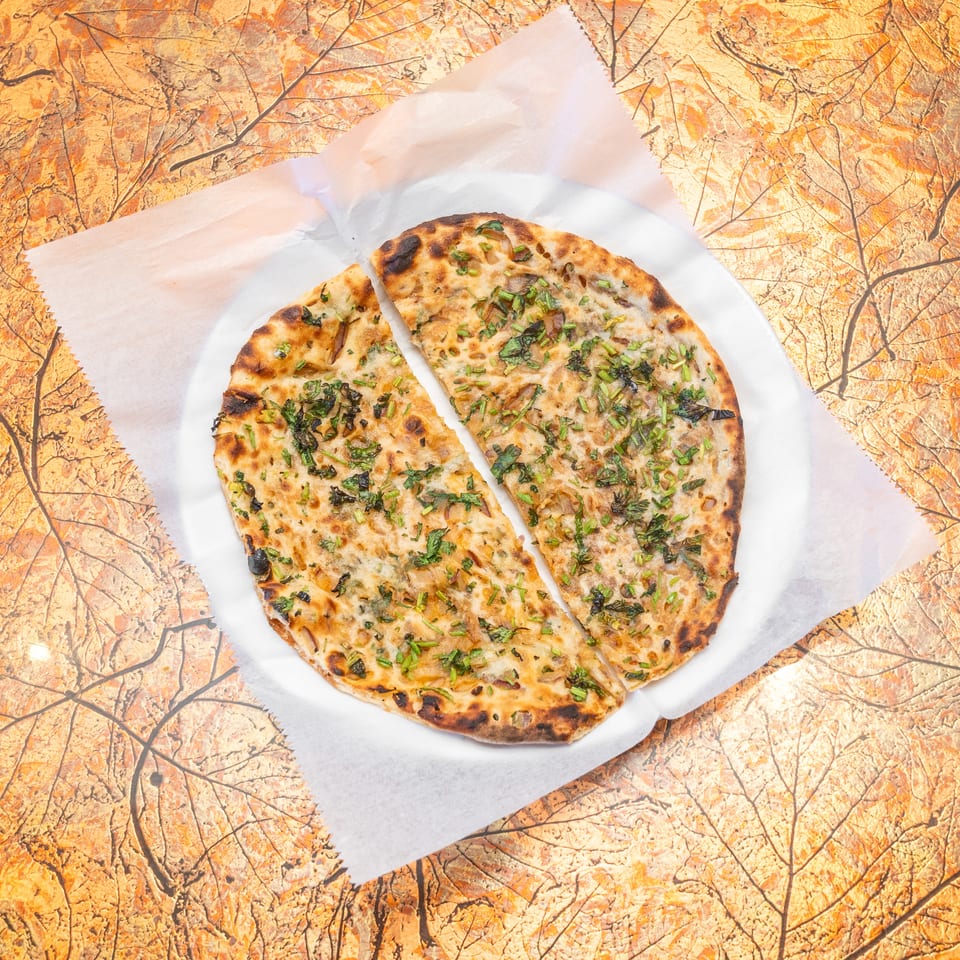 Grilled flatbread topped with chopped fresh herbs, sliced into wedges, and served on parchment over a warm marbled table.