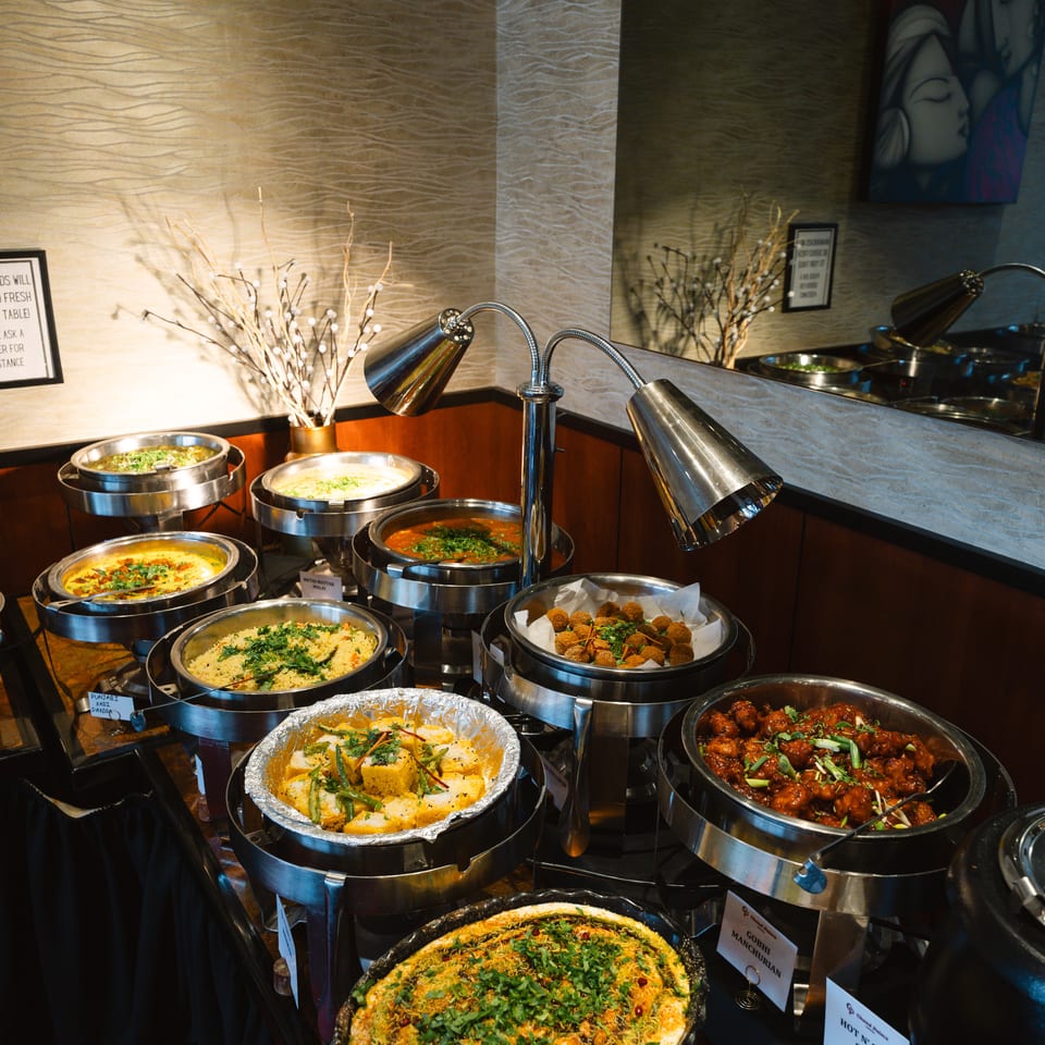 Restaurant buffet displays assorted hot dishes in chafing pans, including casseroles, vegetables, and sauced entrees under heat lamps.