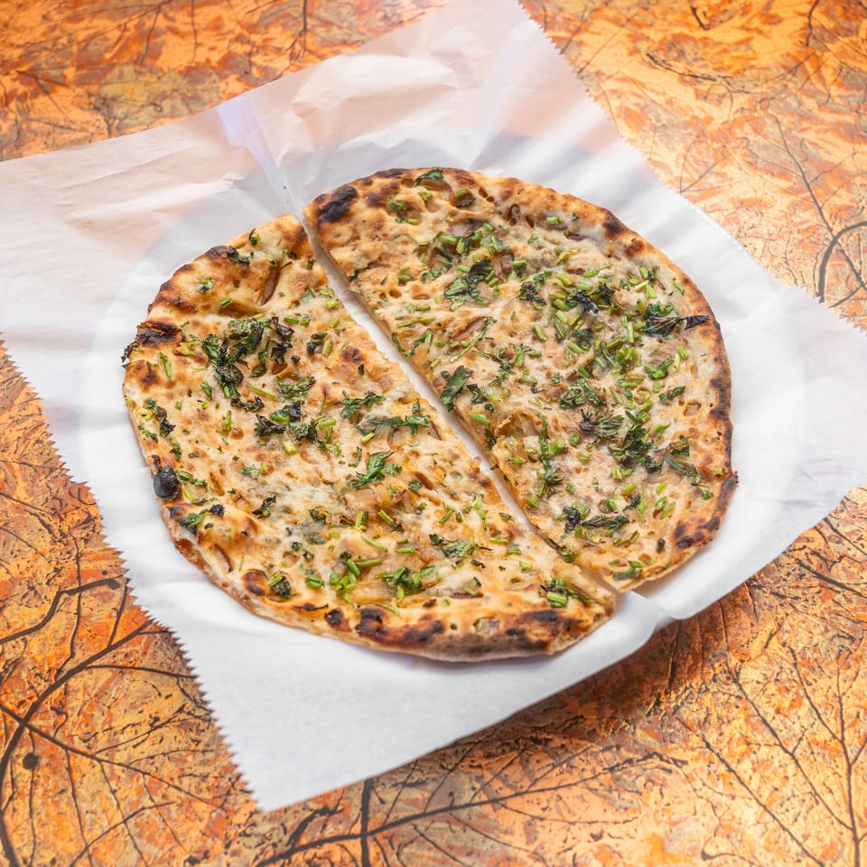 Grilled flatbread topped with fresh herbs, served on white parchment over an autumn leaf-patterned table.