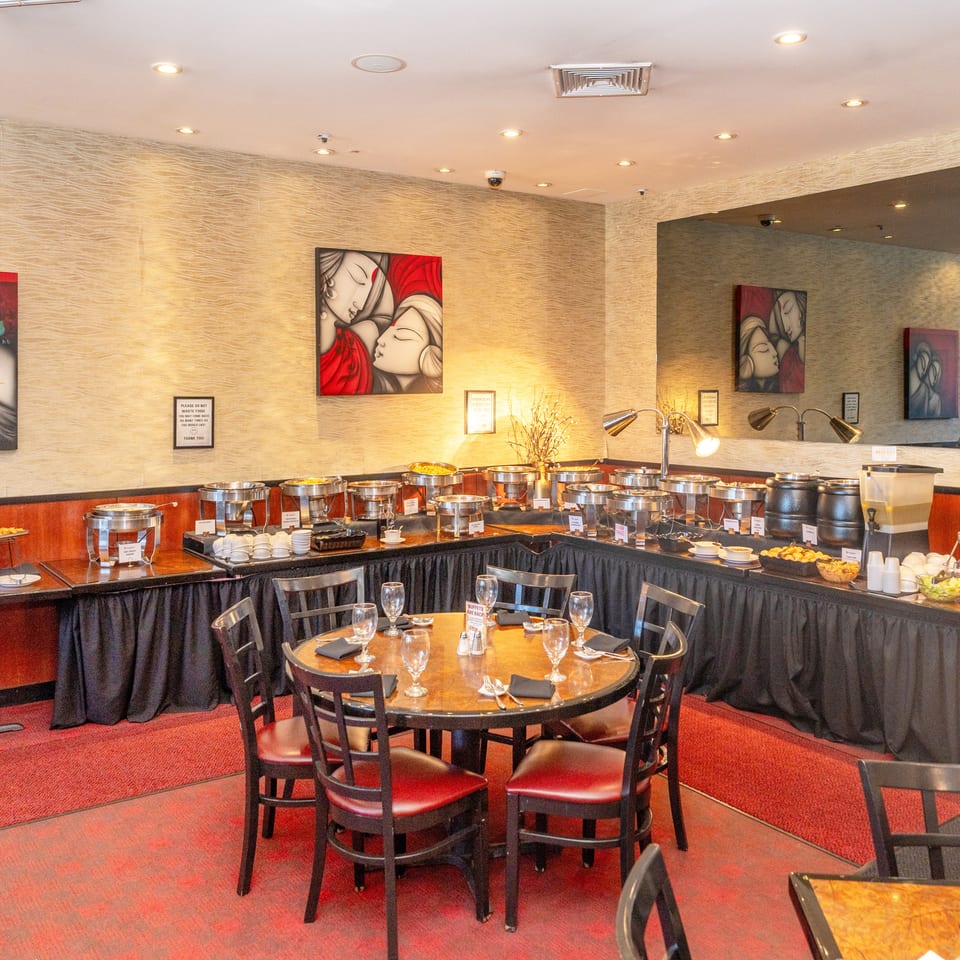 Restaurant dining room with round tables, buffet stations filled with dishes, red carpeting, and decorative artwork.
