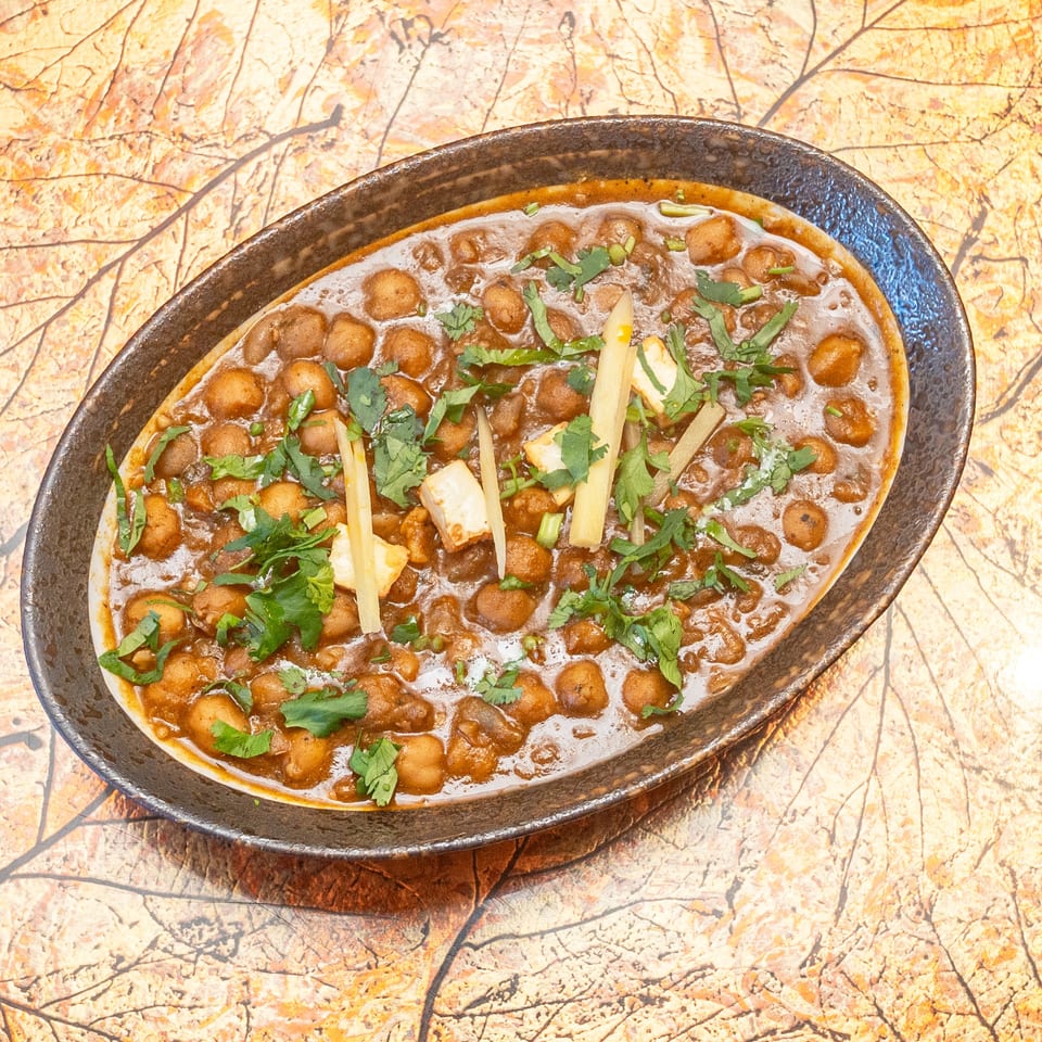 Bowl of spiced chickpea curry garnished with cilantro and ginger strips on a rustic patterned tabletop.