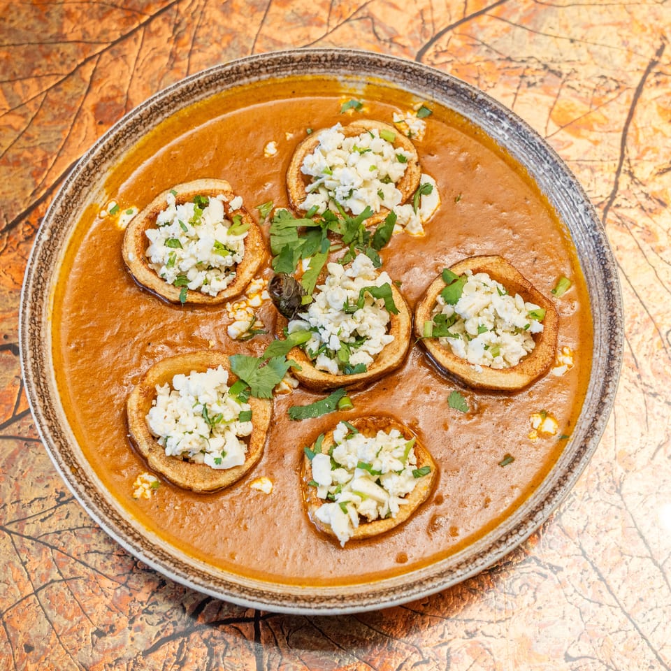 Overhead view of crispy tortillas topped with crumbled white cheese and cilantro in a rich red sauce.
