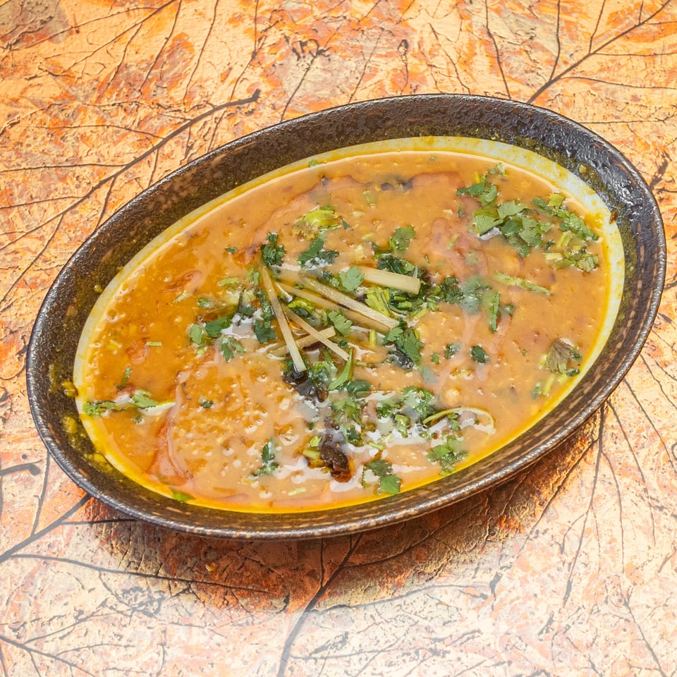 Bowl of orange-brown soup garnished with cilantro and sliced vegetables on a rustic marbled tabletop.