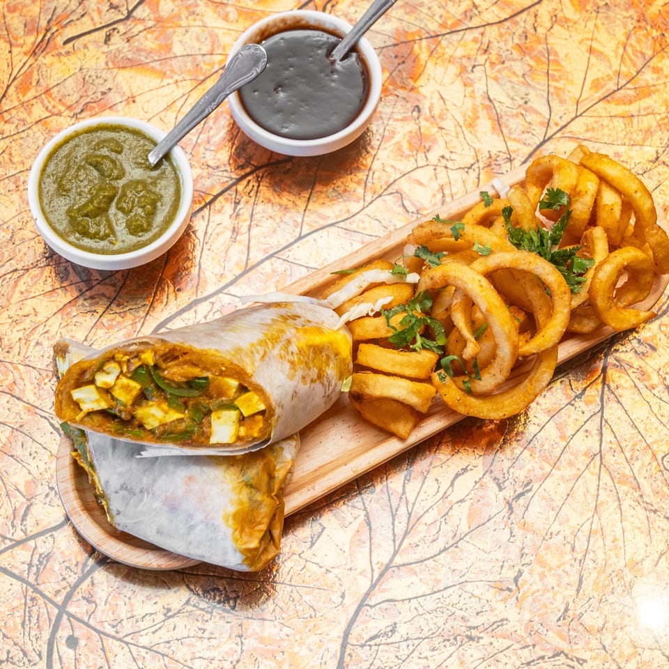 Burrito platter with fries and onion rings, garnished with cilantro, alongside bowls of green and dark dipping sauces.